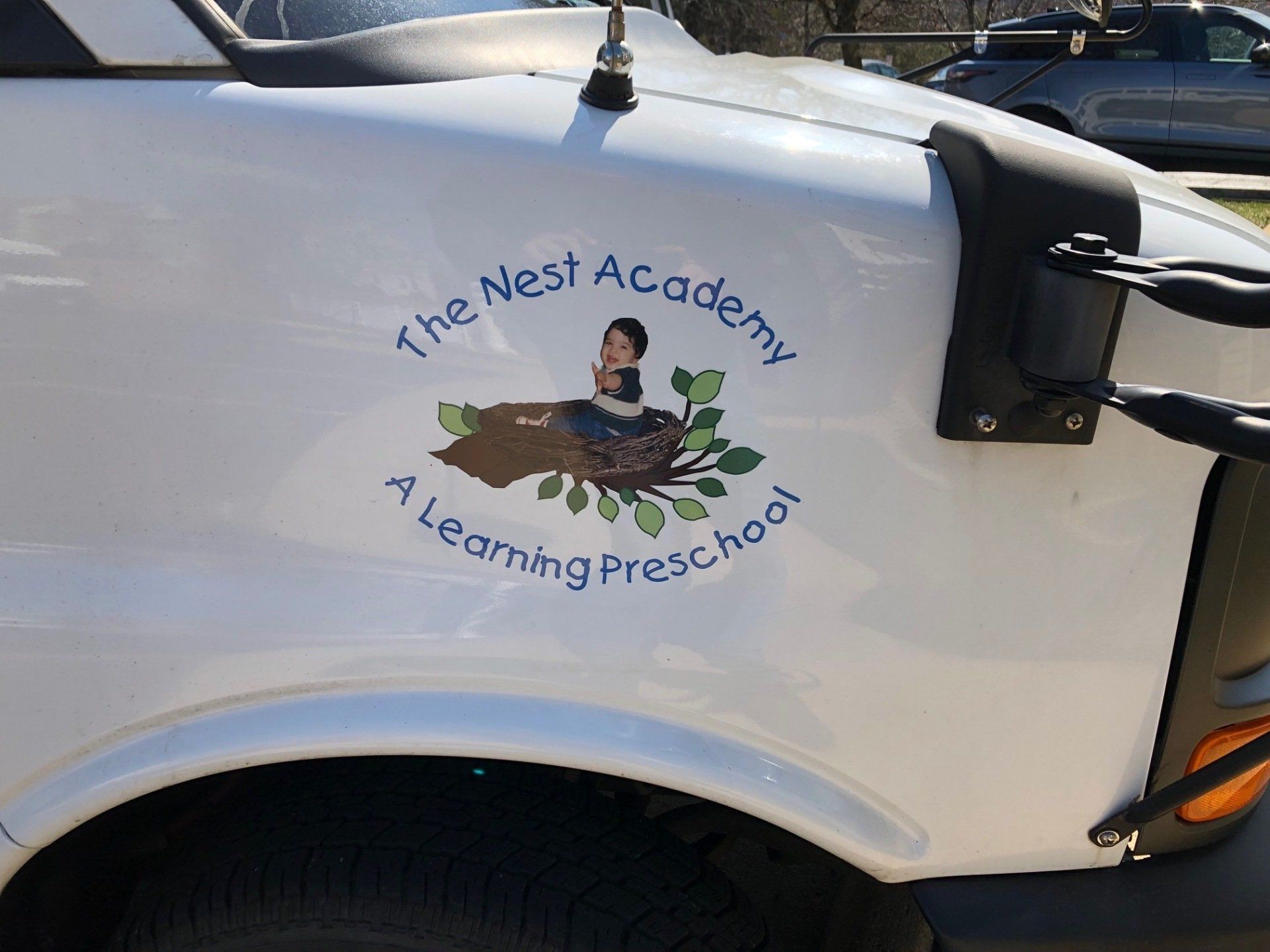 A white truck with a sticker on the side that says the nest academy a learning preschool