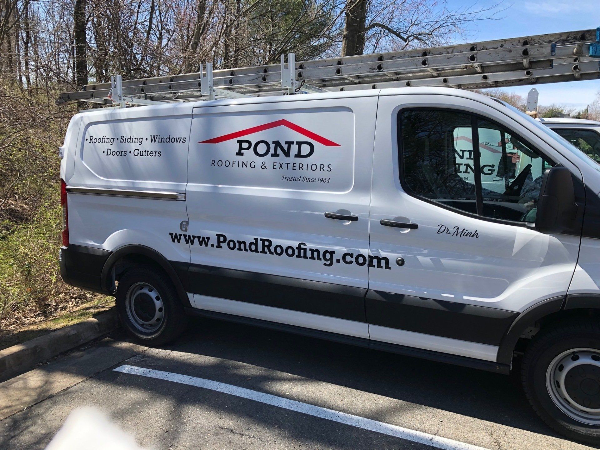 A white van with pond roofing written on it is parked on the side of the road.