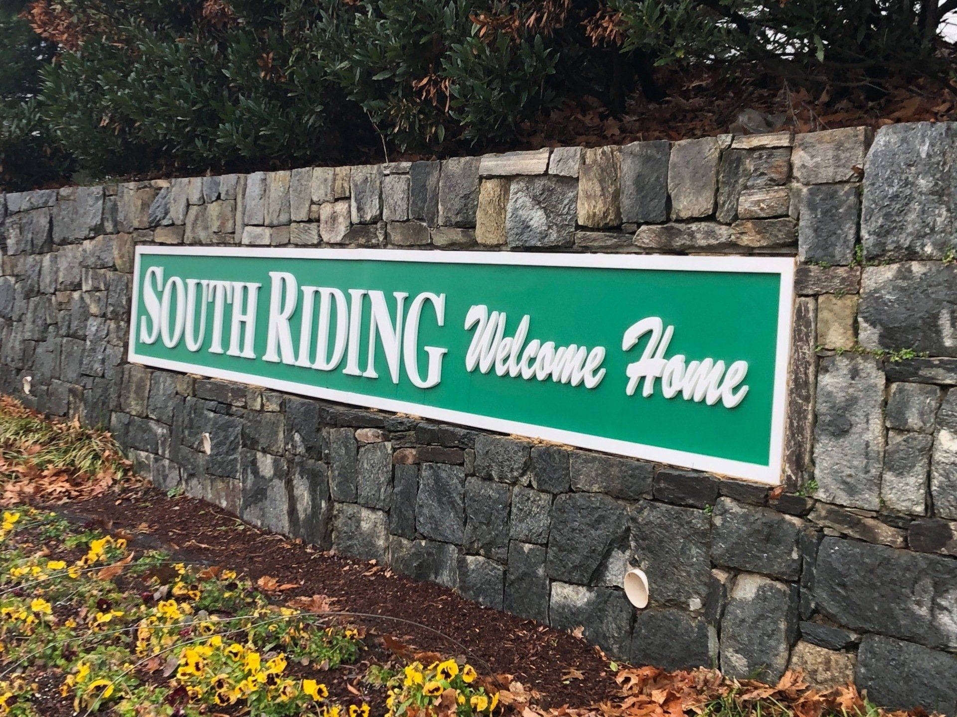 A stone wall with a green sign that says south riding welcome home