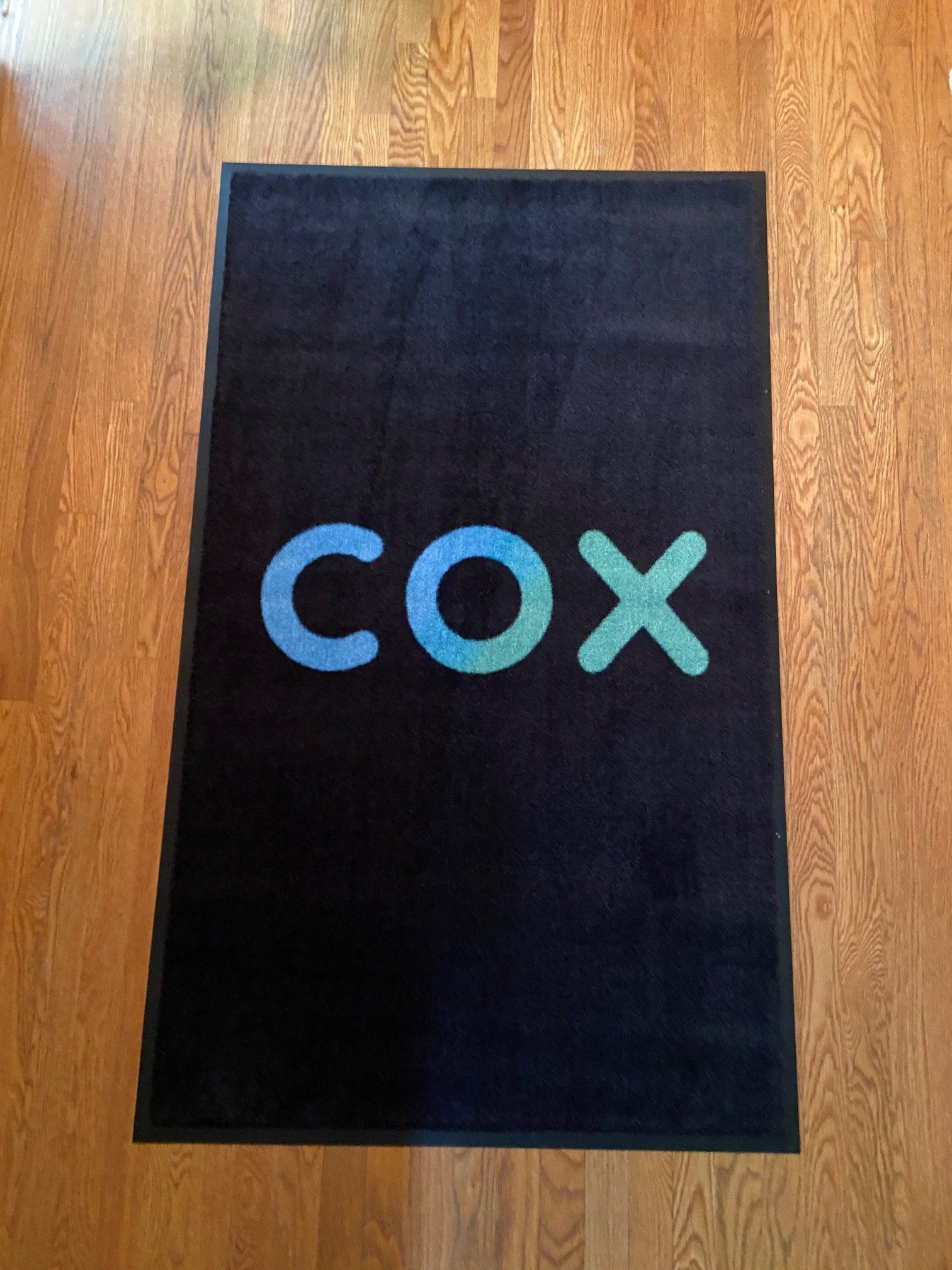 A black rug with the word cox on it is on a wooden floor.
