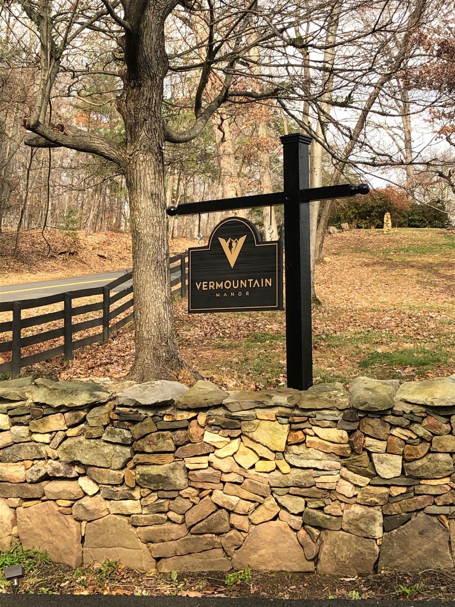 A sign on a pole next to a stone wall.