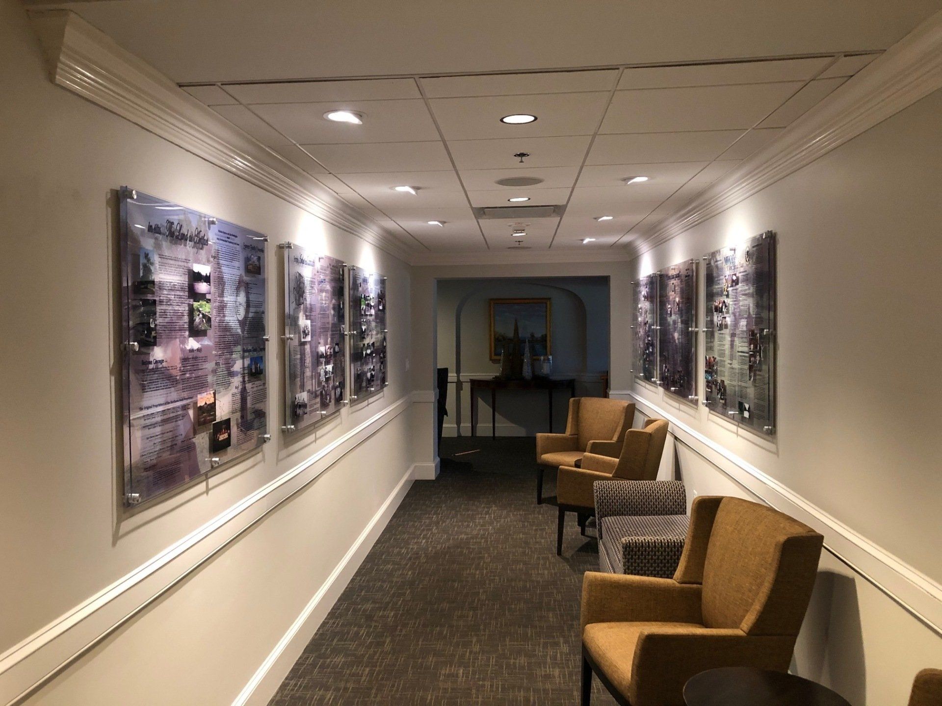 A long hallway with chairs and paintings on the wall.