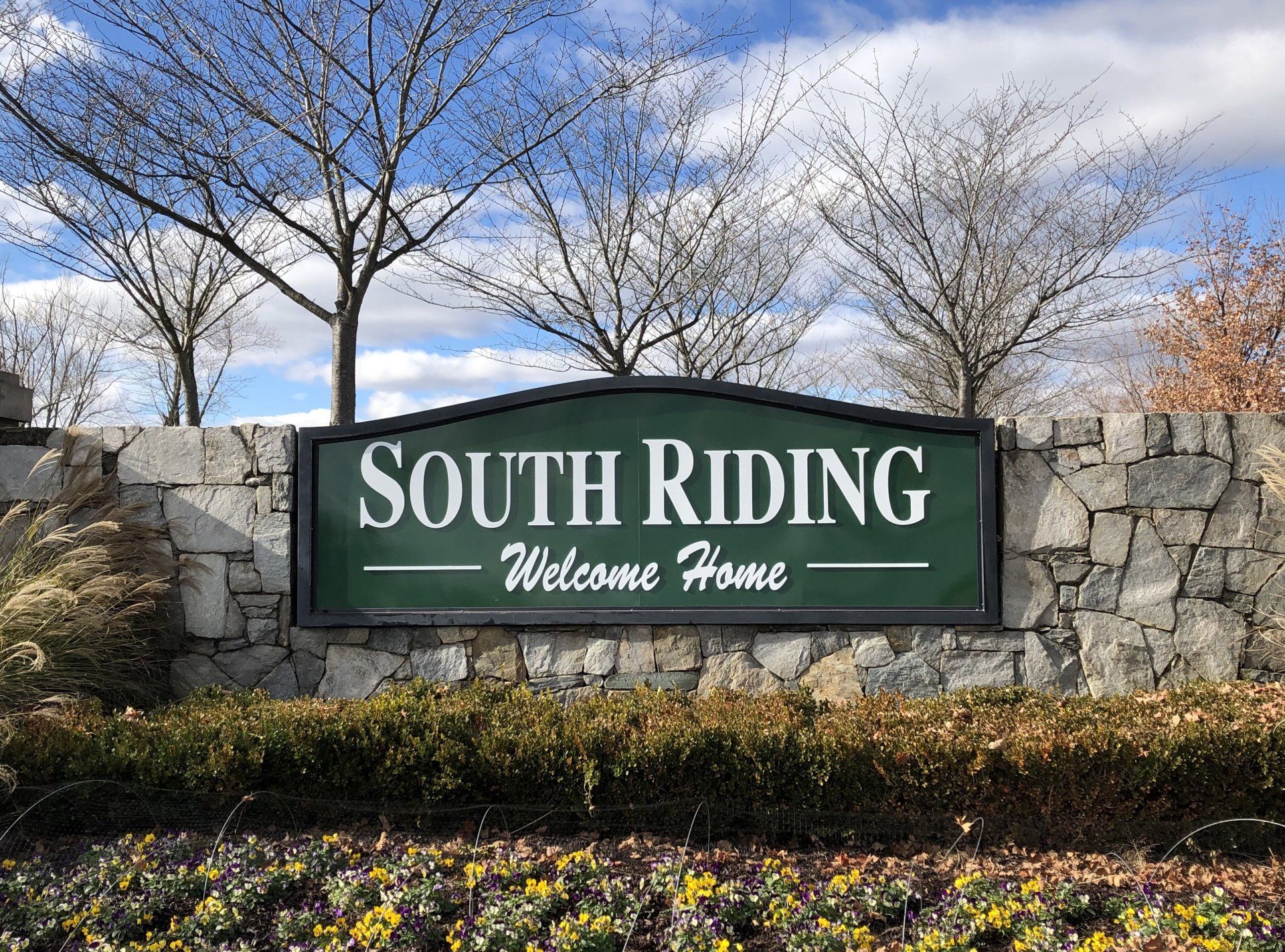 A green sign on a stone wall says south riding welcome home.