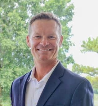 A man in a blue polo shirt is smiling for the camera.