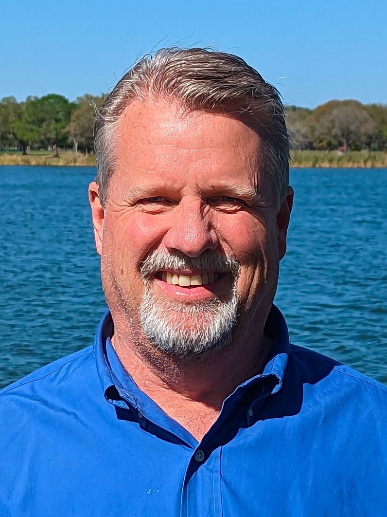 A man in a blue polo shirt is smiling for the camera.