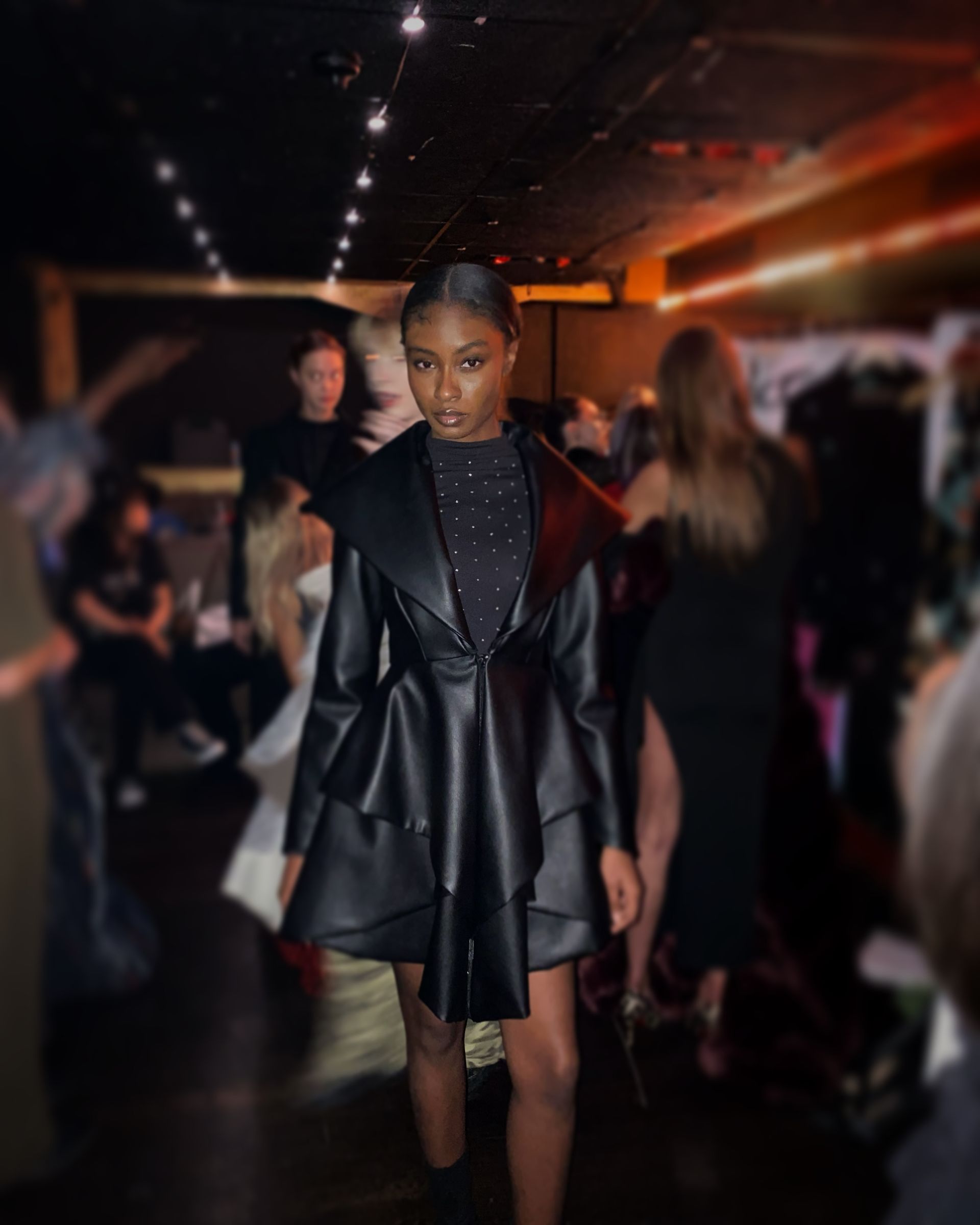 Fashion model in a black leather jacket, walking the runway.