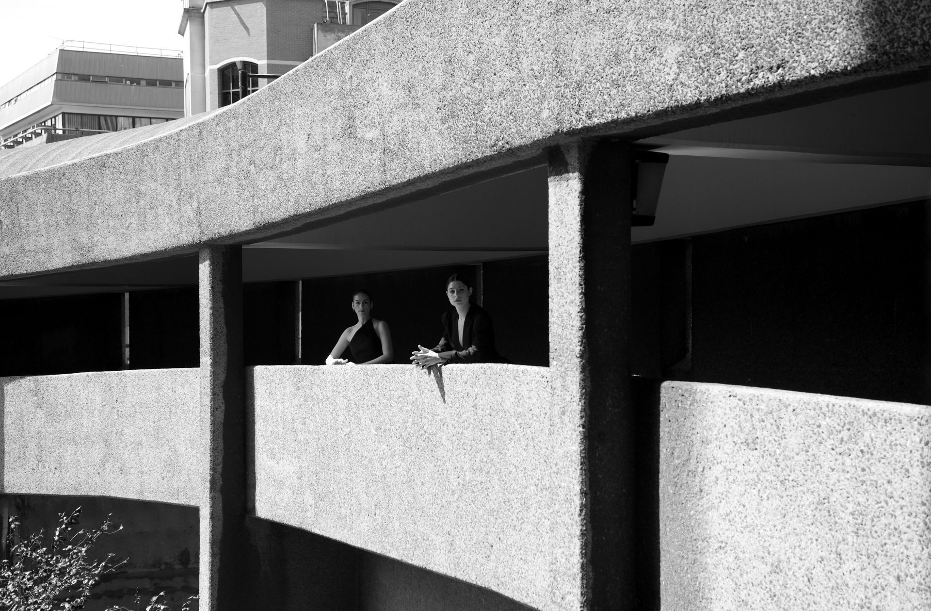 Two people stand on a curved balcony of a concrete building, looking outwards.