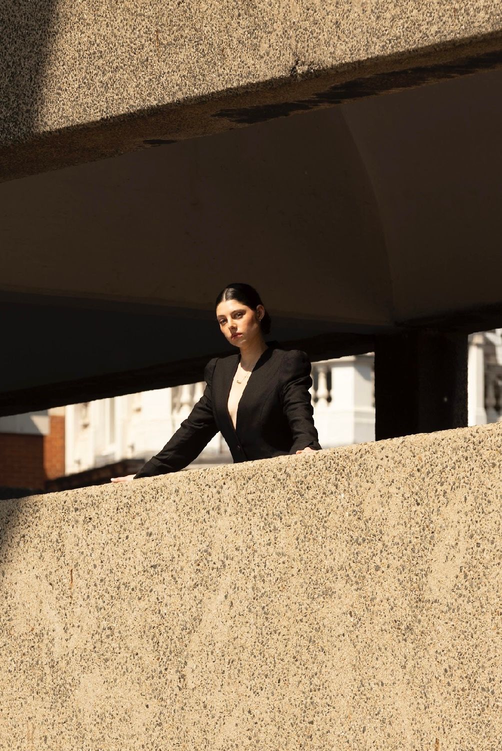 Woman in black blazer stands on a concrete ledge, looking toward the camera.
