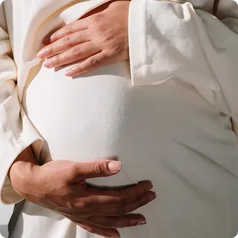 Person in light clothing, holding their pregnant belly.