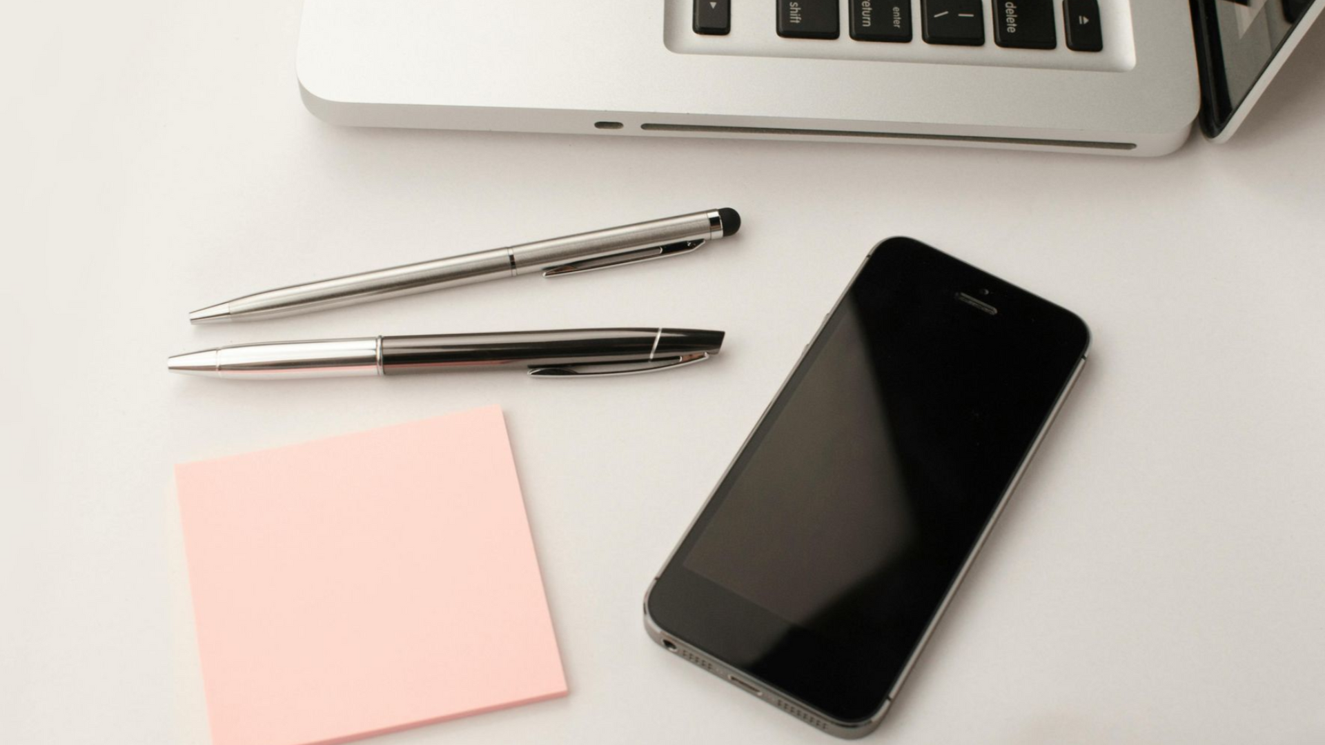 Laptop, smartphone, pens, and sticky notes on a white surface.