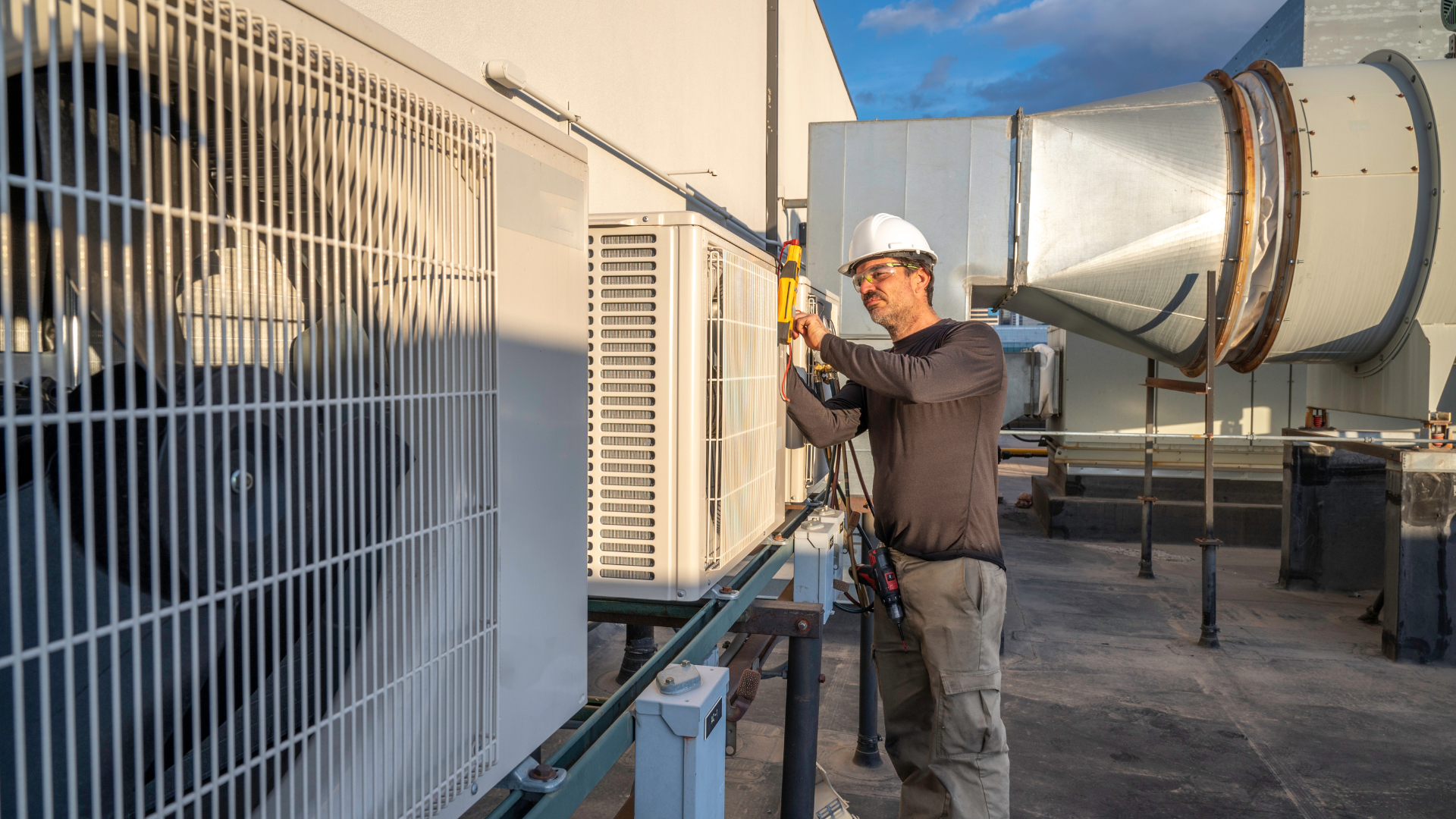 A man is working on an air conditioner on the roof of a building.