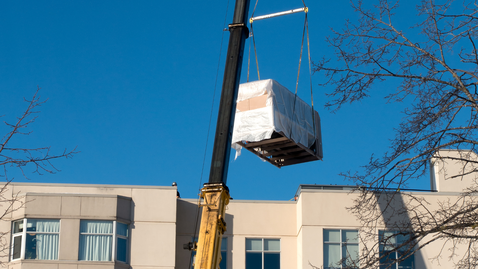 A crane is lifting a large white box over a building.