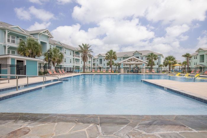 Swimming pool with turquoise apartment buildings under a cloudy sky.