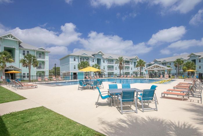 Pool area at apartment complex: turquoise buildings, pool, seating, sunny day.