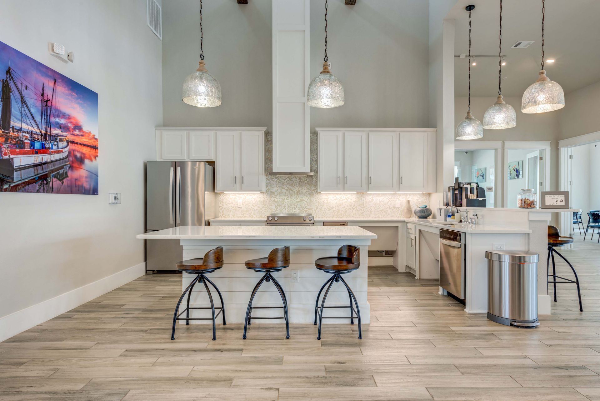A modern white kitchen with island, bar stools, pendant lights, and artwork.