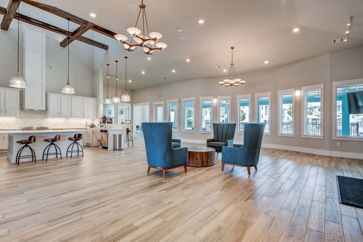 Spacious, bright room with light wood floors, kitchen, seating area. Blue armchairs around a wood table near windows.