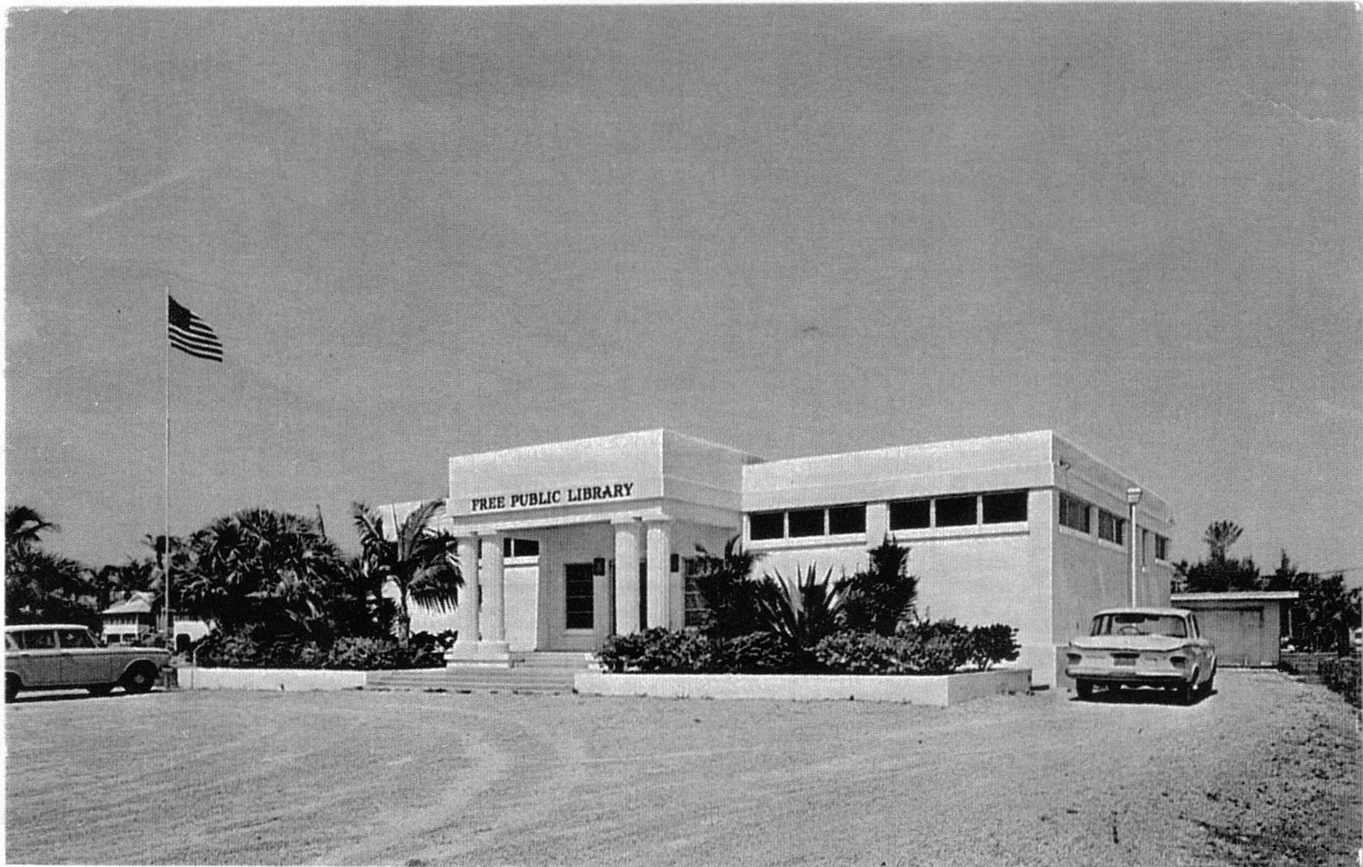A black and white photo of a large white building with cars parked in front of it