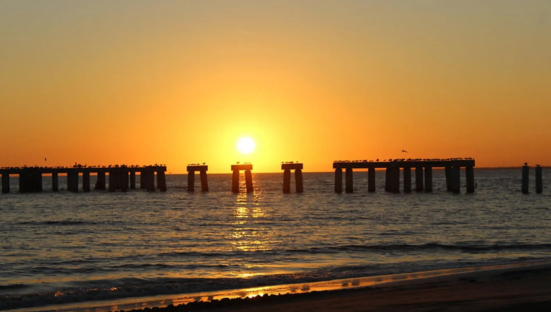 A sunset over the ocean with a pier in the foreground