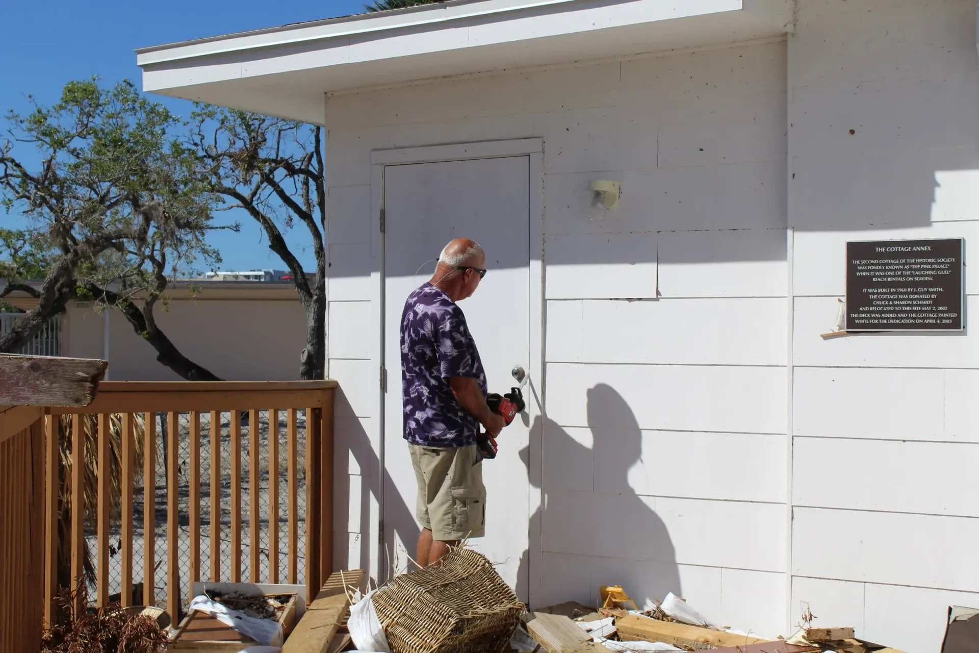 A man in a purple shirt is standing in front of a white building