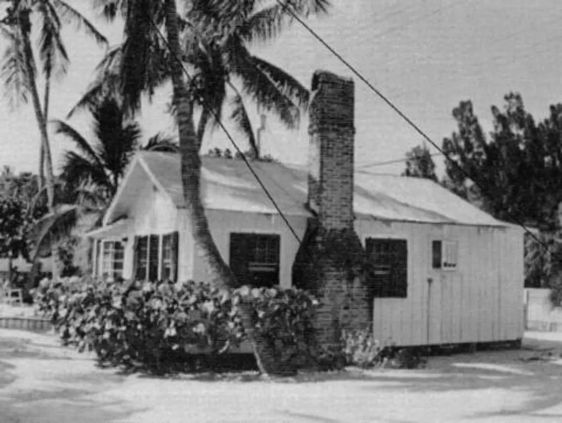 A black and white photo of a house with palm trees in the background