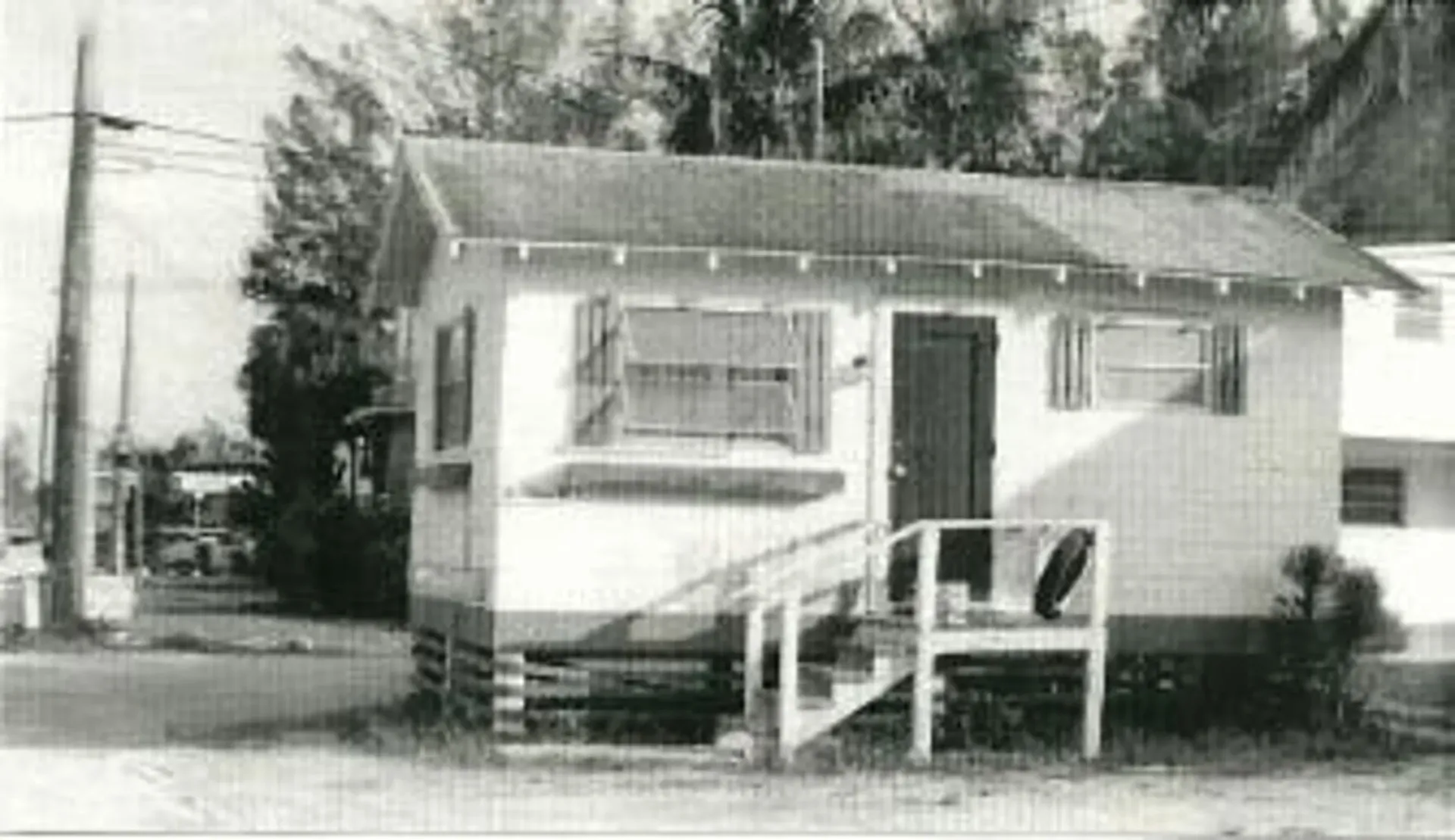 A black and white photo of a small house with stairs leading up to it.