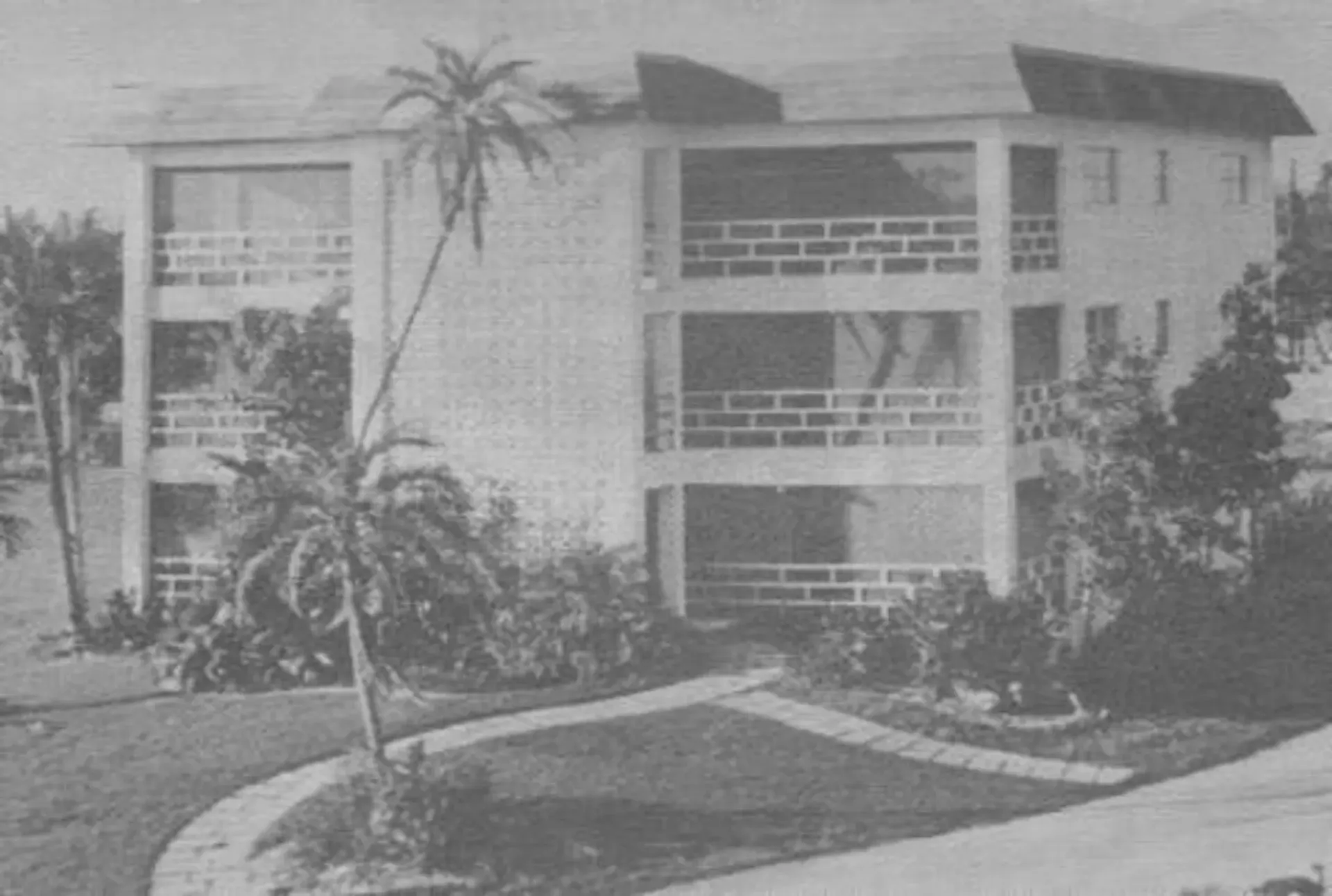 A black and white photo of a building with palm trees in front of it