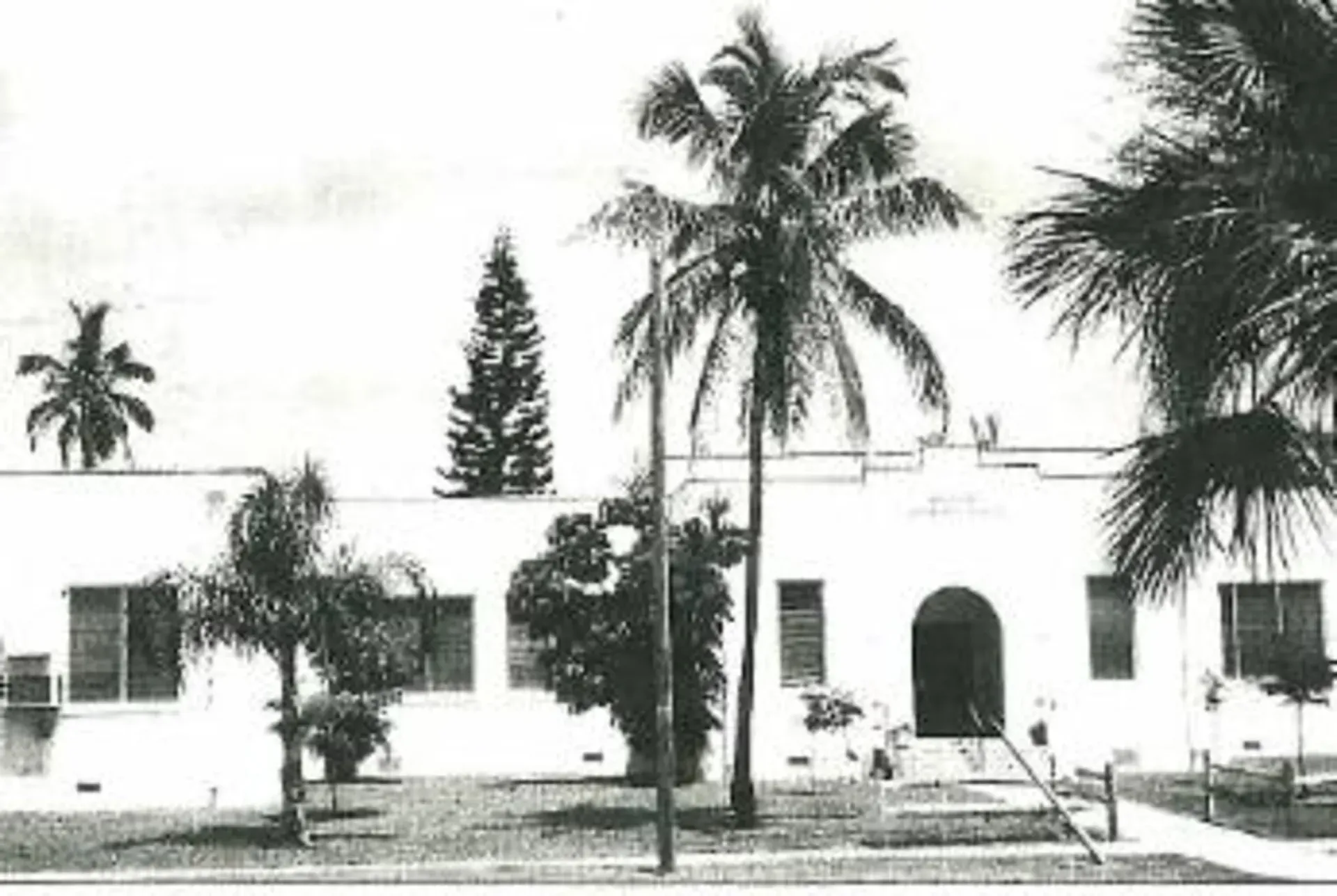A black and white photo of a house with palm trees in front of it