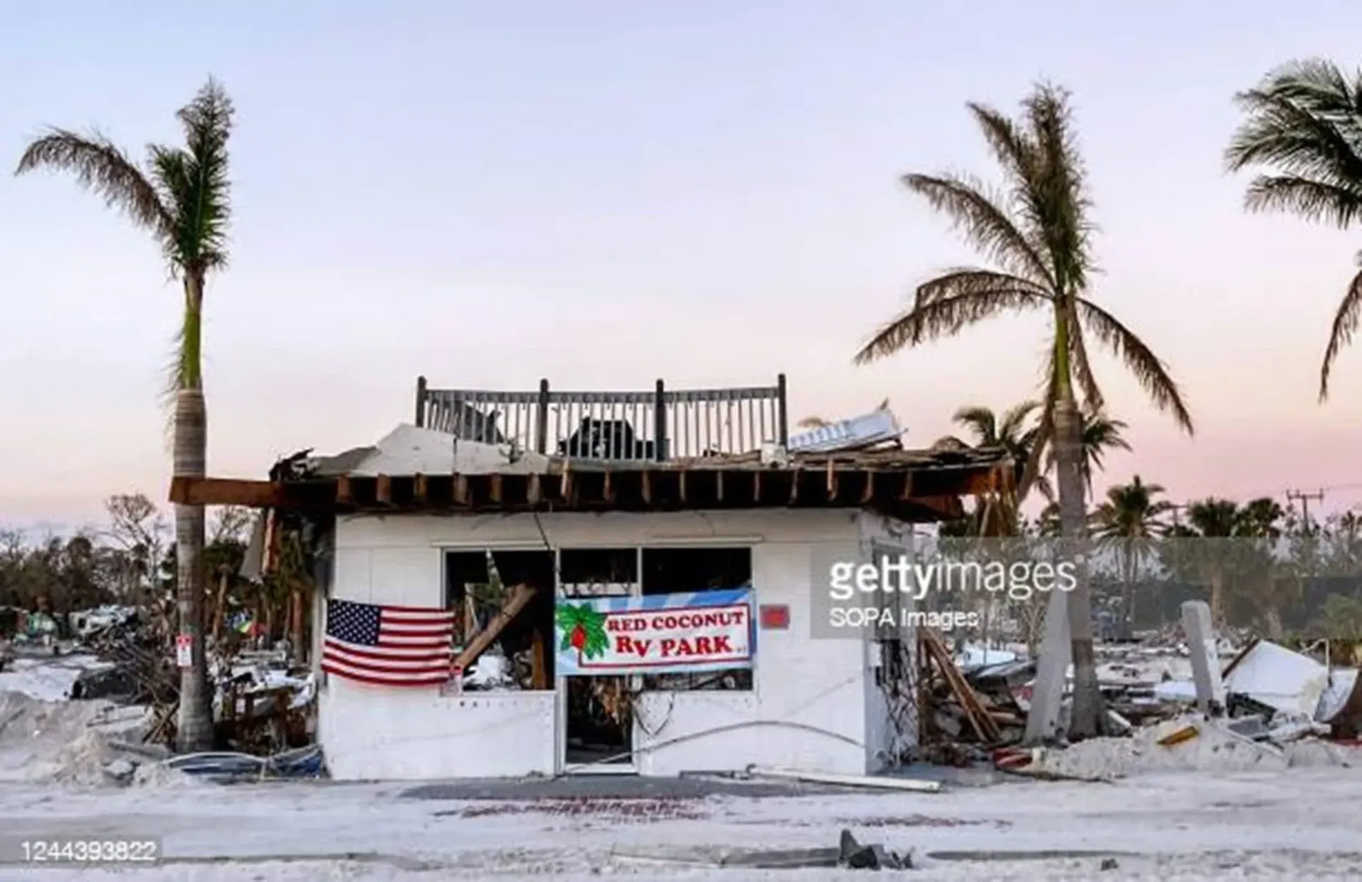 A white building with palm trees in the background and an american flag on the side.