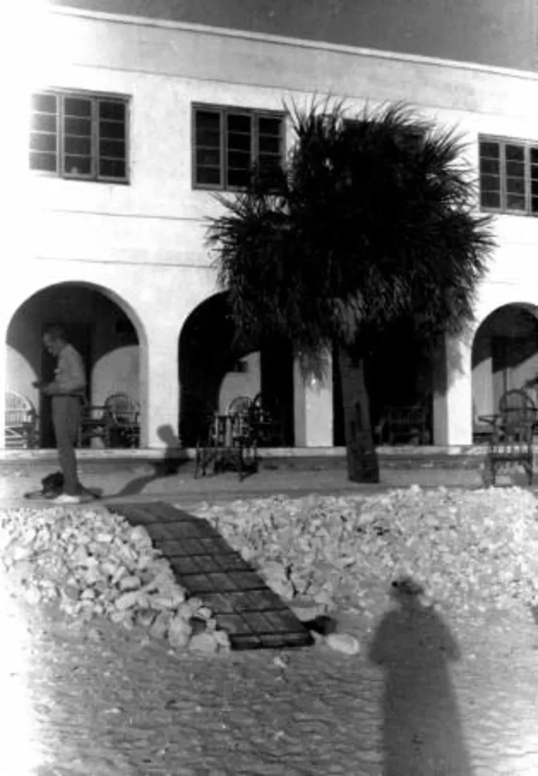 A black and white photo of a man standing in front of a building