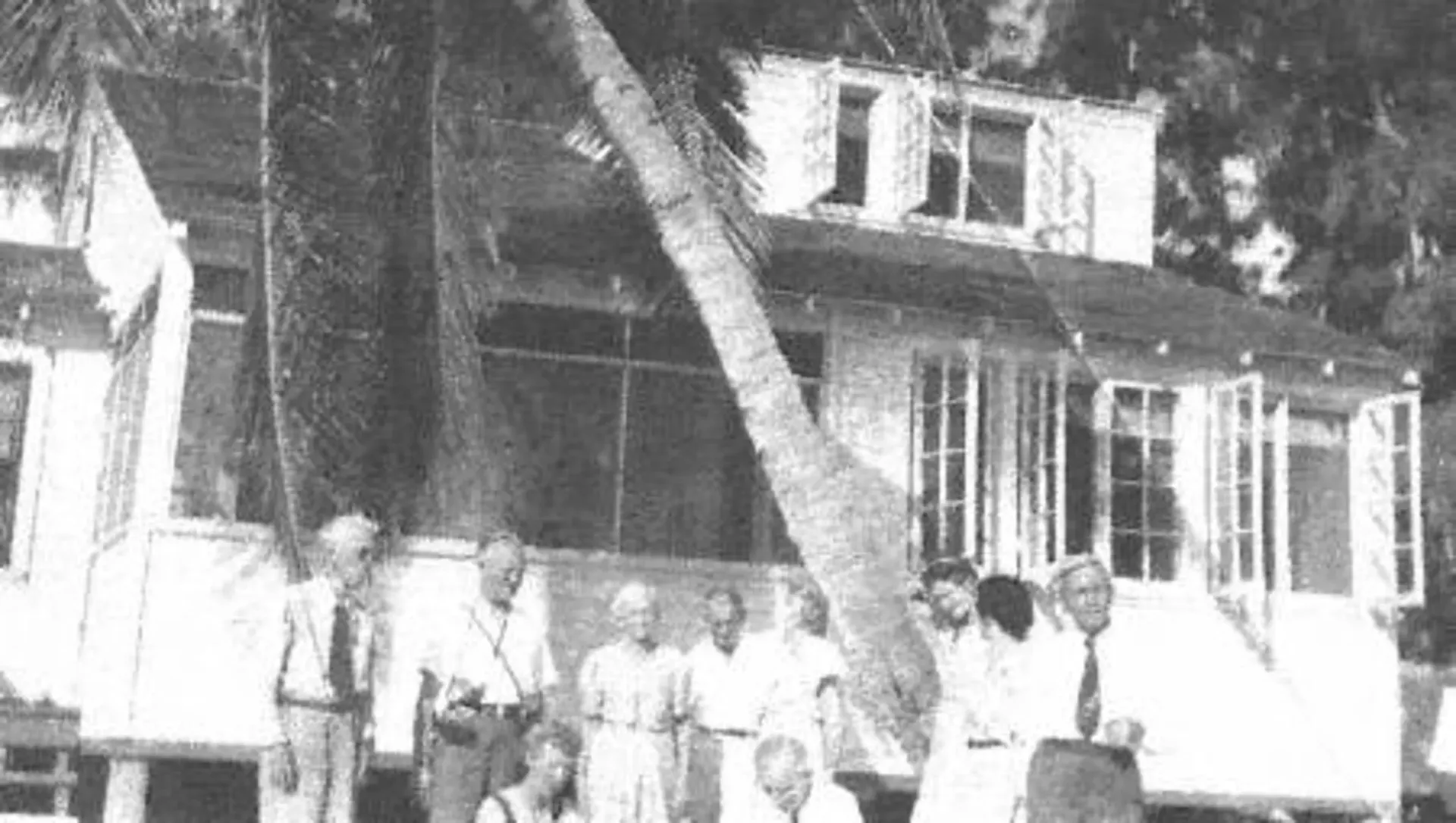 A black and white photo of a group of people standing in front of a house.