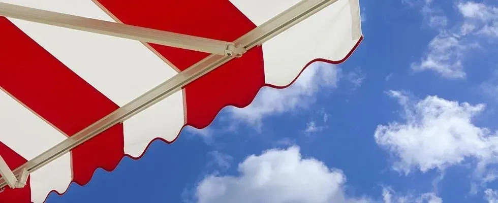 Tenda a strisce rosse e bianche contro un cielo azzurro con nuvole soffici.