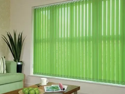 Tende verticali verdi su una finestra; nella stanza ci sono un divano verde e una pianta.