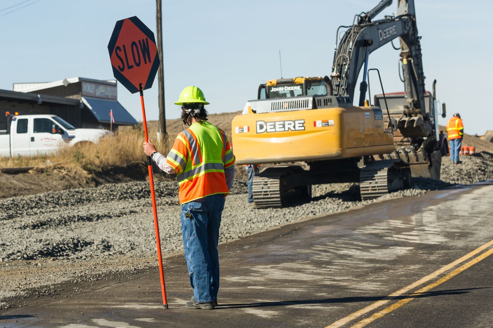 Traffic control flagger managing highway construction work zone with heavy equipment and roadway safety signage