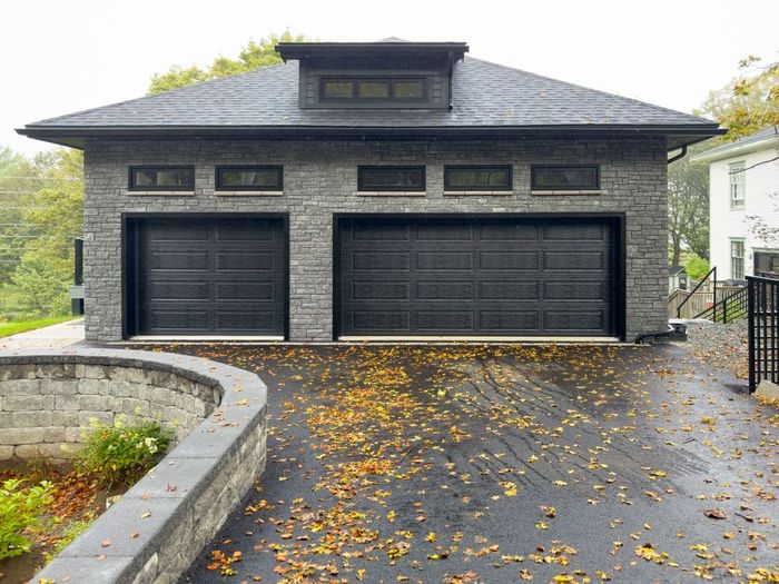 A garage with two black garage doors and a driveway filled with leaves.