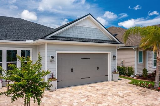 A white house with a gray garage door and a palm tree in front of it.