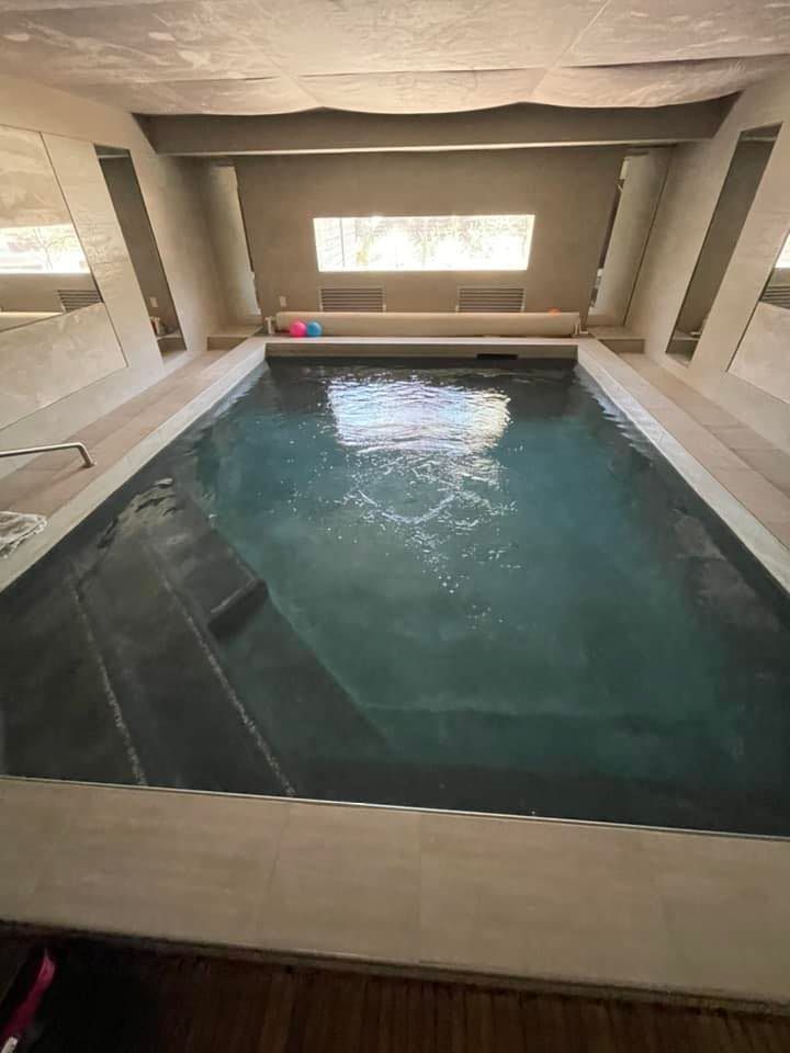 Indoor pool with gray steps, water, and light-toned walls. Two colorful balls float.