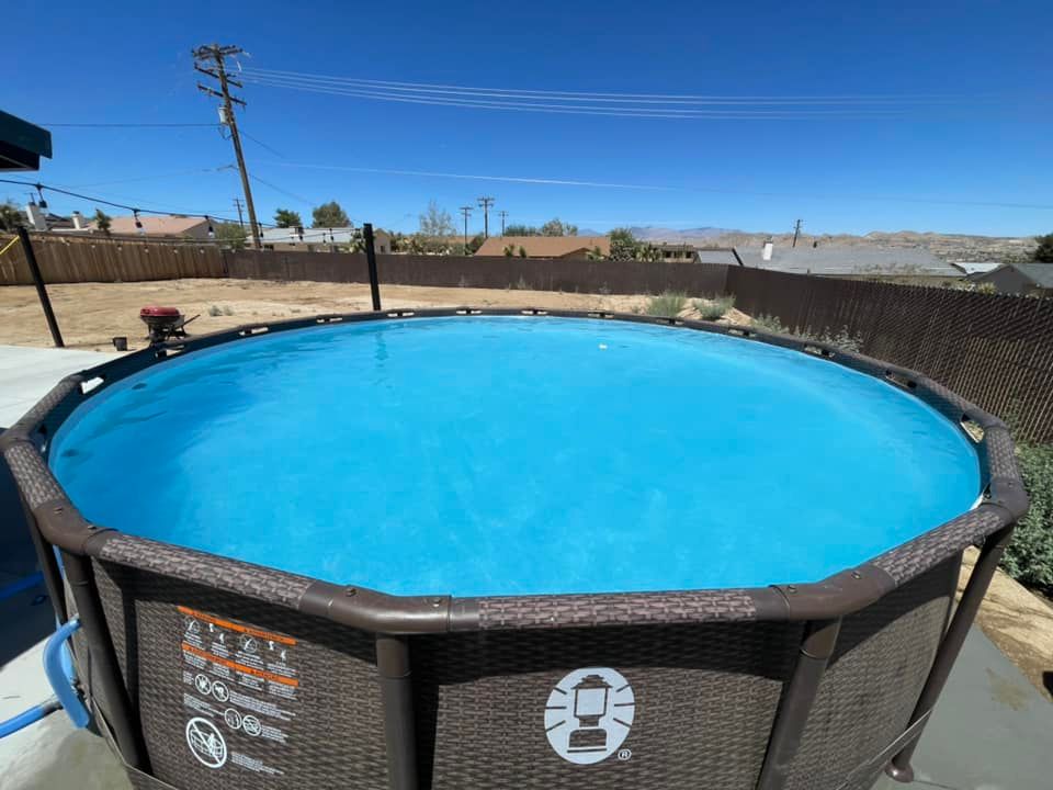 Above-ground circular pool filled with blue water. Brown frame, clear sky, fenced yard.