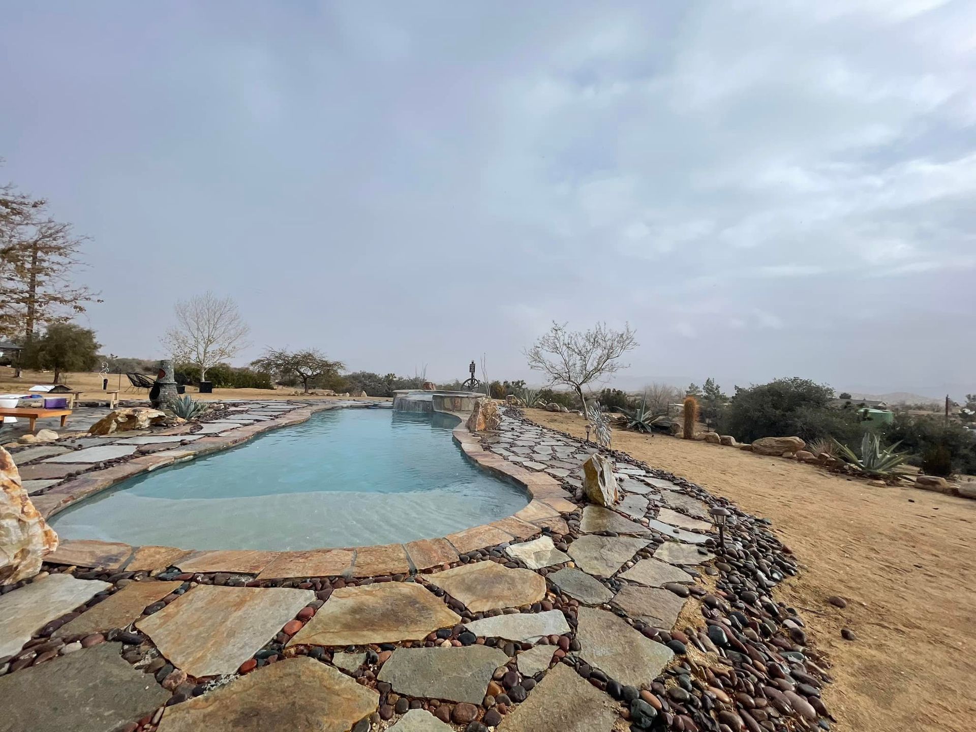 Outdoor pool with stone border under a cloudy sky.
