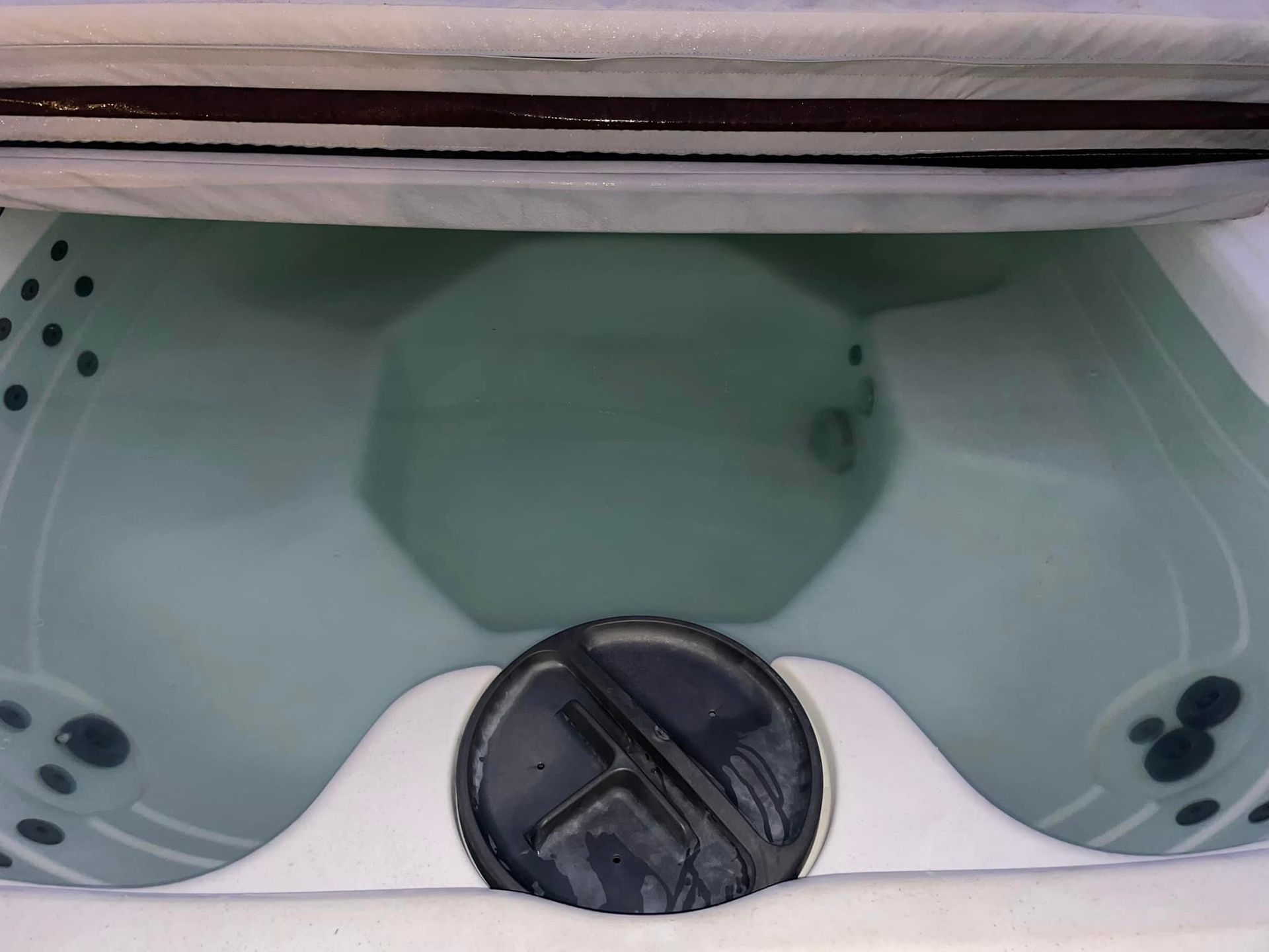 A partially filled hot tub with a dark circular drain cover, and jets along the sides.