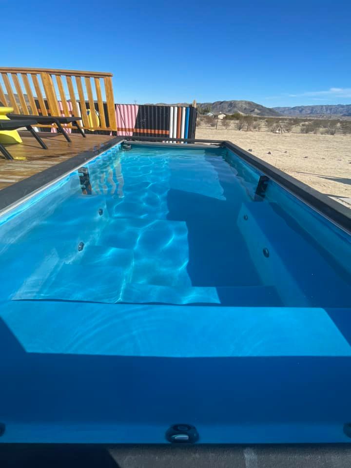 Rectangular blue pool, surrounded by decking, in a desert landscape under a clear blue sky.