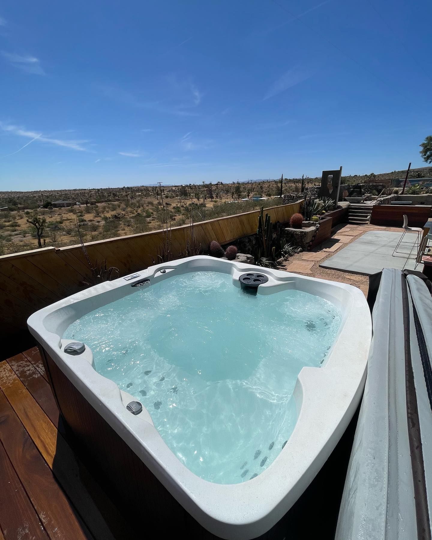 Hot tub filled with bubbly water, outdoor deck with desert landscape in the background under a blue sky.