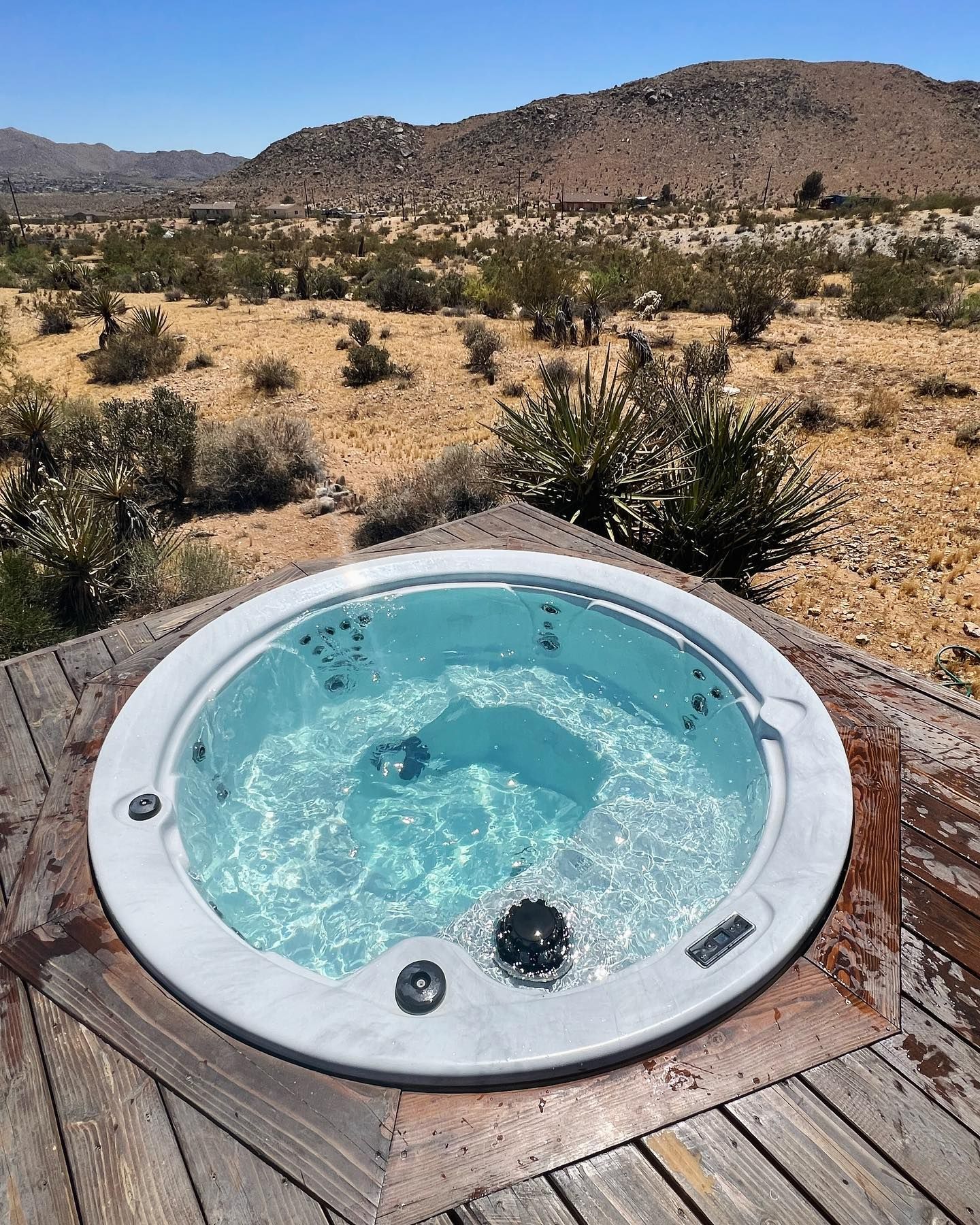 Hot tub filled with water, on a wooden deck, desert landscape in the background.