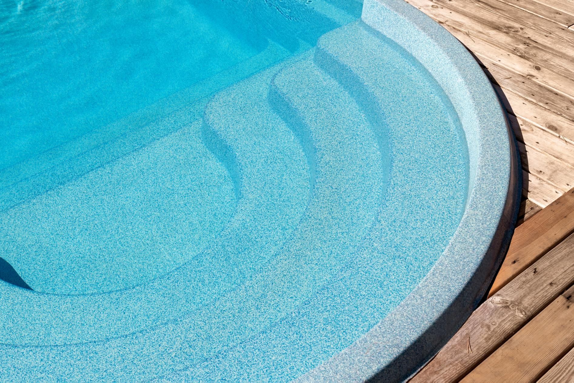 Curved blue pool with steps next to a wooden deck.