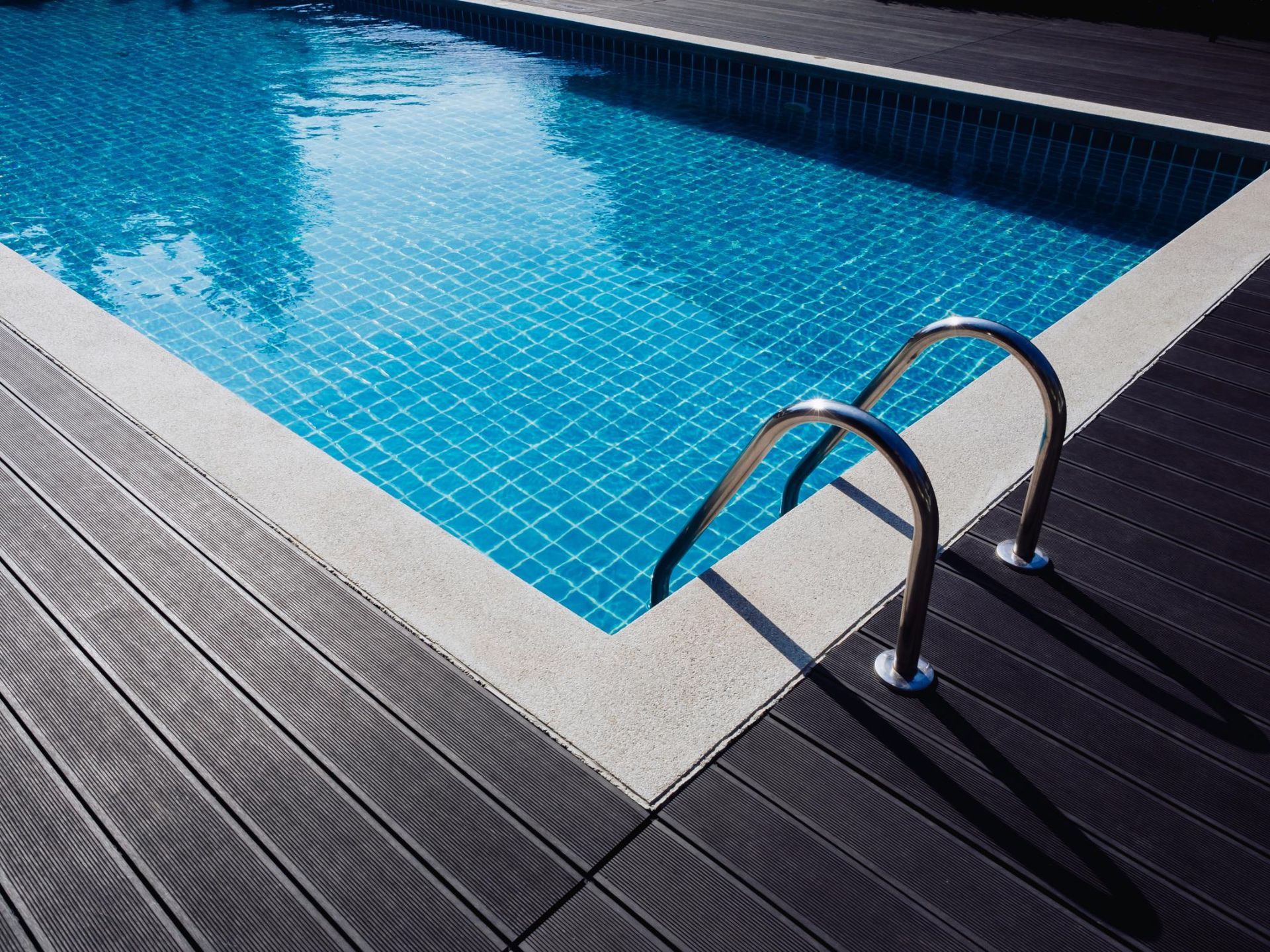 Pool with blue water and metallic ladder, surrounded by gray wooden decking.