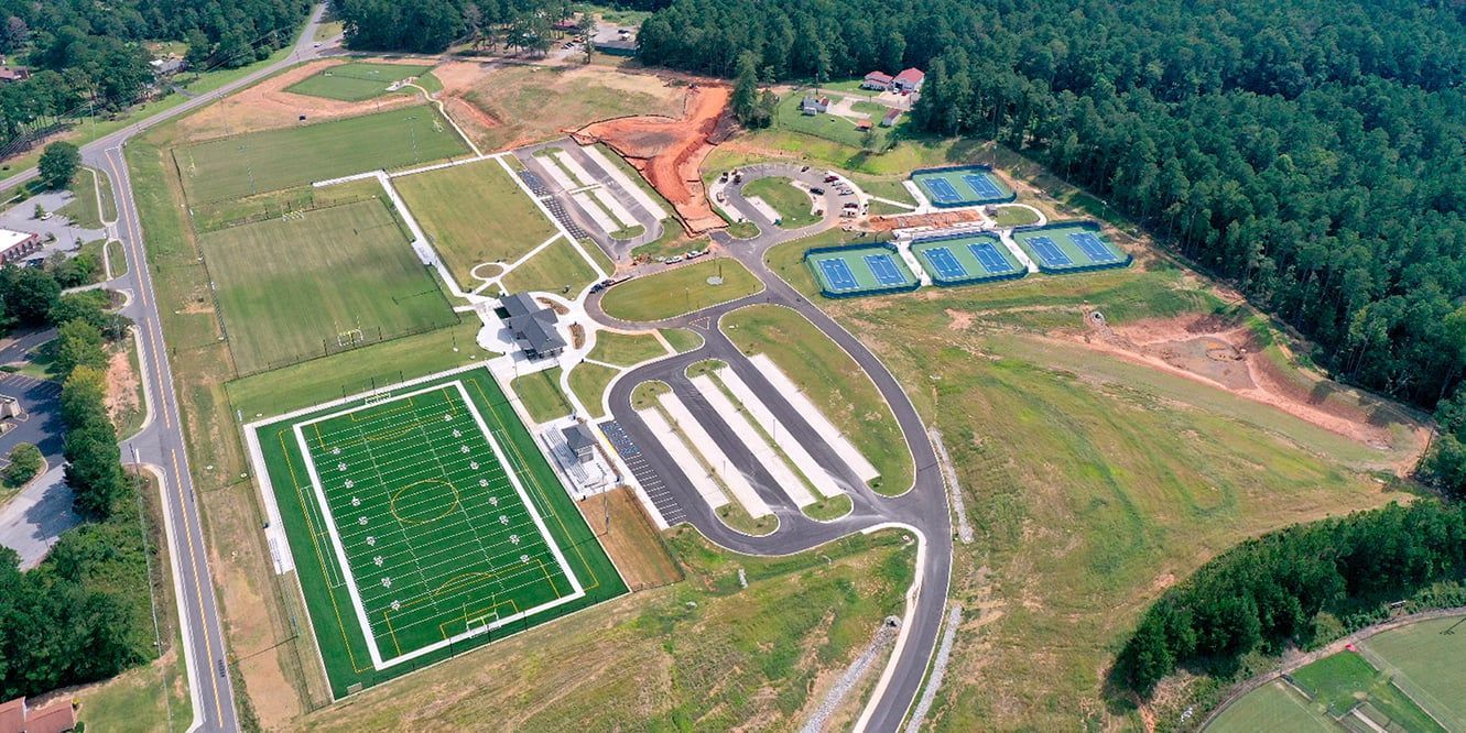 Aerial view of a sports complex with a football field, tennis courts, and parking.