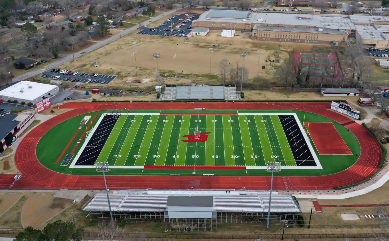 Aerial view of a football field with a red running track and surrounding buildings.