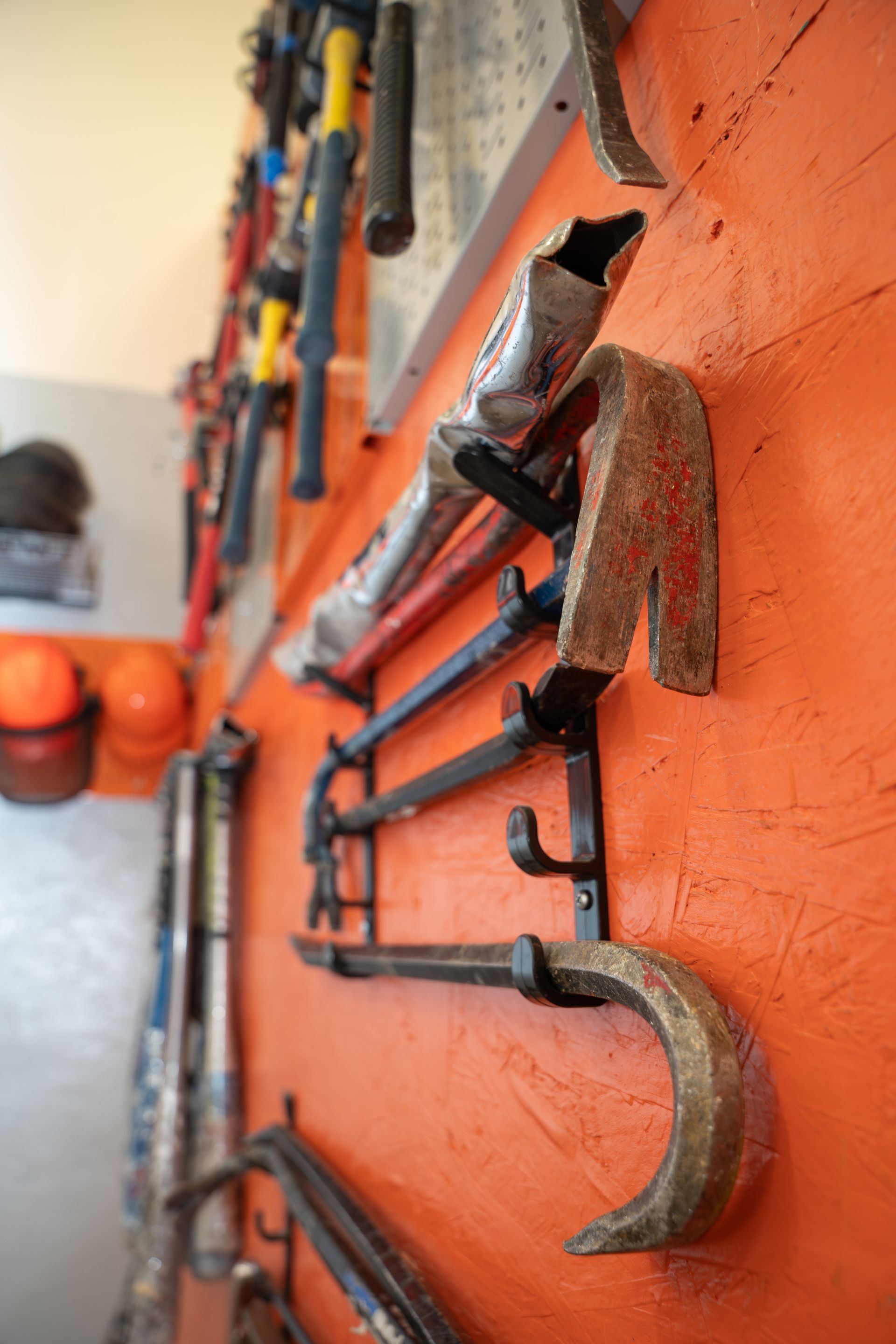 Orange wall with hand tools, including pry bars, mounted on holders.