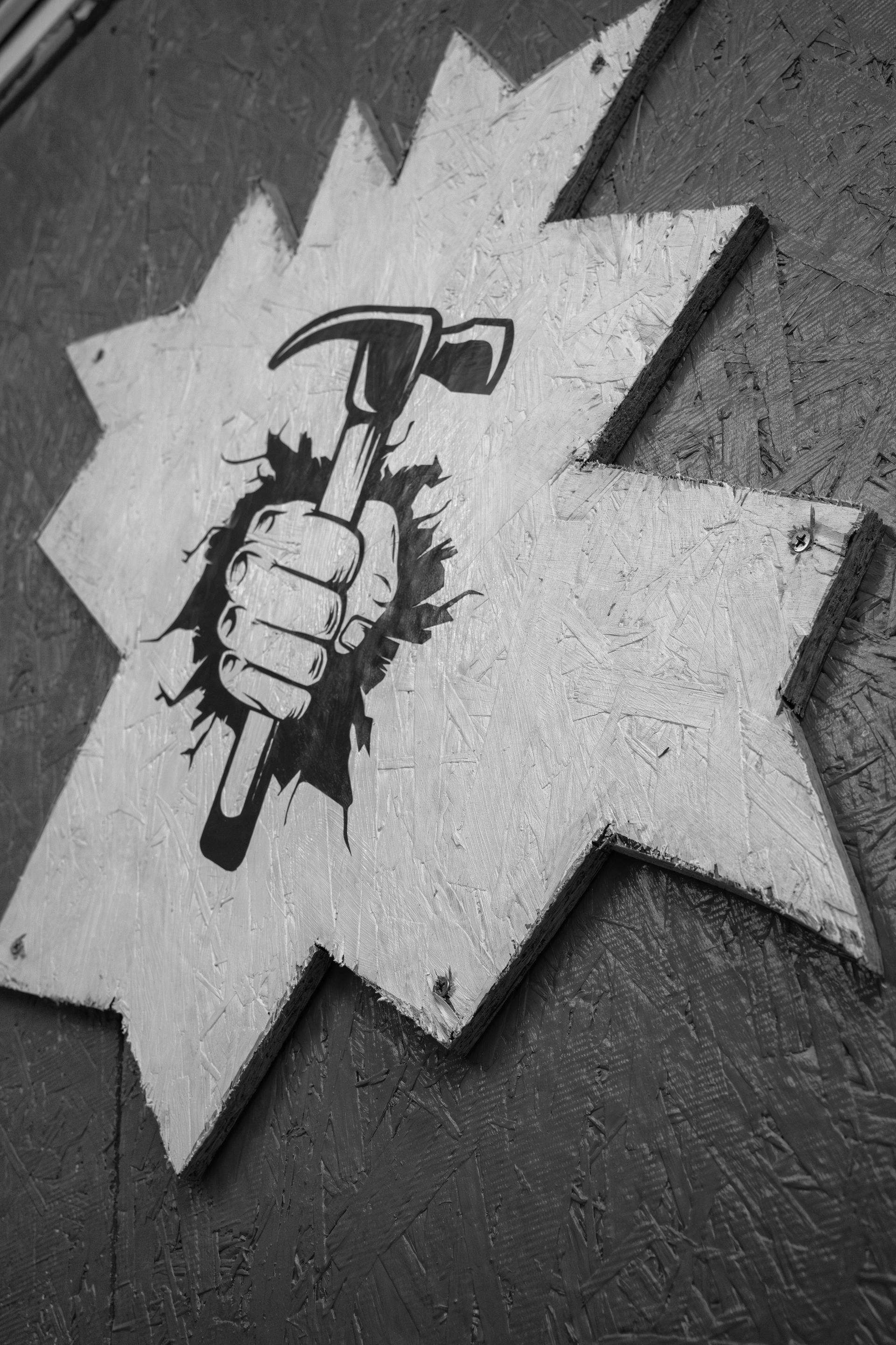 Hammer held in a clenched fist bursting through a star-shaped sign. Black and white.