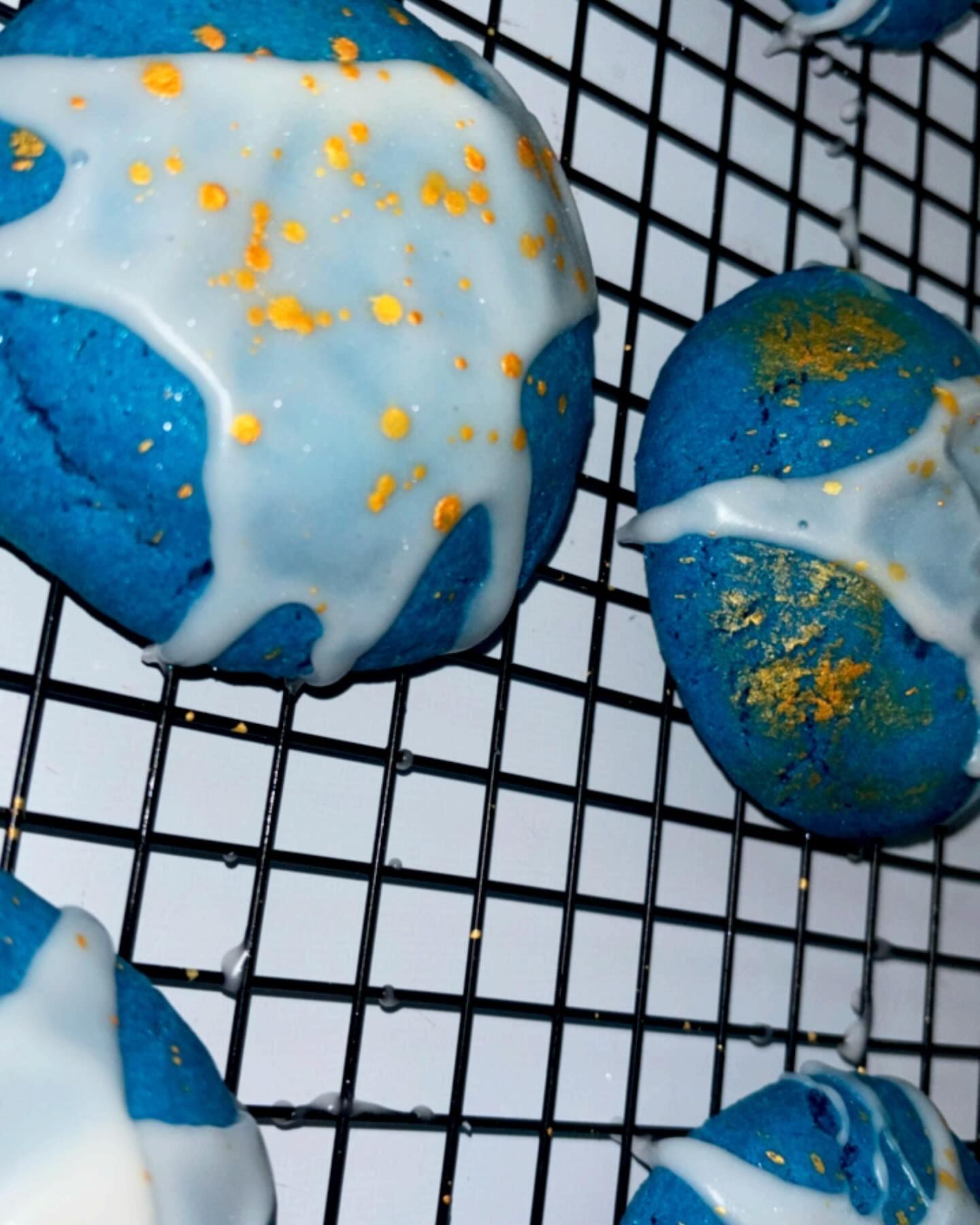 Blue cookies with white glaze and gold sprinkles on a black wire rack.