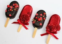 Four gourmet popsicles arranged in a row, alternating between black chocolate and red glitter finishes with floral decor.